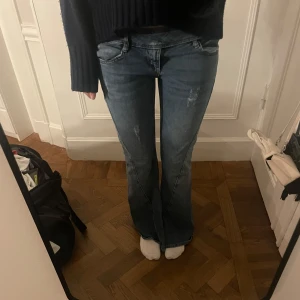 Blå bootcut jeans - Säljer ett par snygga blå bootcut low waist jeans i bra skick. Väldigt unika och fina med en slit över benet som ni ser på bilden! Passar bra till både sneakers och klackar!