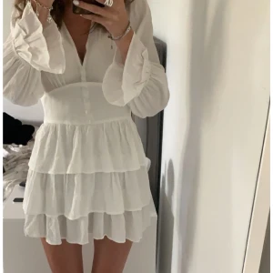 Vit kortklänning med volanger - Säljer en perfekt vit kortklänning med volanger och långa ärmar. 