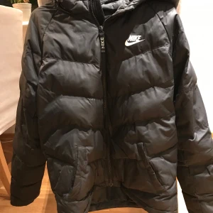 Nike jacka - En svart Nike Jack med små hål och en lagning. Jackan är storlek 158-170 och funkar för höst sen vinter och vår förutom små hålen är jackan helt okej skick.