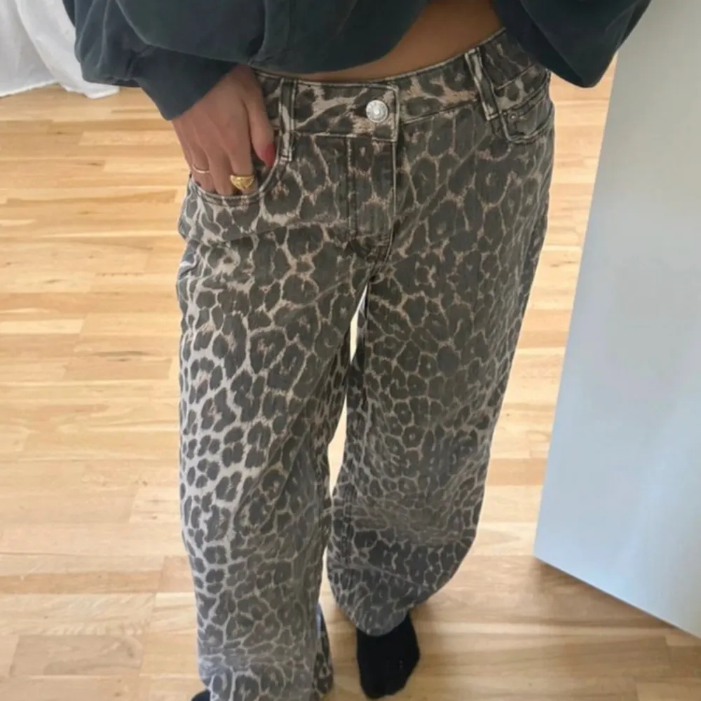 Säljer ett par coola leopardmönstrade jeansbyxor i loose fit. De har en hög midja och knappar framtill. Perfekta för att ge din outfit en trendig touch. Passar både till vardags och fest!. Jeans & Byxor.