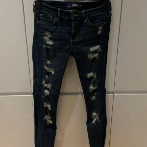 Mörkblå lågmidjade slitna jeans - Säljer ett par mörkblå jeans i storlek L med coola slitningar längs benen. De har en tight passform, lågmidjade!