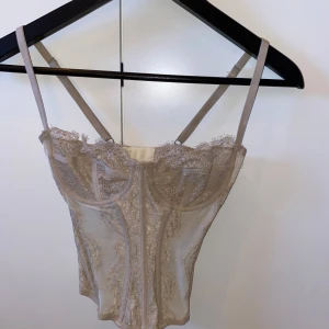 Beige spetskorsett - En beige korsett från Urban outfitters. Toppen har ingen lapp, den köptes utan i butik. Den är i storlek 34 och passar kupa 75a/b. 