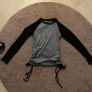 Grå och svart långärmad topp - Säljer en snygg grå och svart långärmad topp med snörning i sidorna. Perfekt för en casual look eller en utekväll. Toppen är i bra skick och har en tight passform som framhäver figuren. Den är superbekväm och lätt att matcha med jeans eller kjol. Passa på att fynda! Priset går att diskuteras🩷🩷