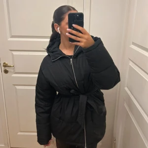 Svart jacka med knytning i midjan från Nelly - Vinterjacka, köpt förra året för 560kr. Modellen heter Precious Puffer Jacket på hemsidan men är slutsåld i de flesta storlekar!   Behövs en omgång tvätt och fickorna har spruckit (som ses på bild, syns också att jag sytt ihop dom vilket också spruck