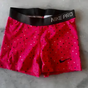 Säljer ett par rosa träningsshorts från Nike Pro i mycket bra skick. De har ett coolt prickigt mönster i svart och vitt och en bred, svart resårmidja med Nike Pro-loggan. Perfekta för träning och sommaraktiviteter! 🏋️‍♀️