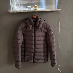 Grå dunjacka från Colmar - Säljer en snygg grå dunjacka från Colmar i mycket bra skick. Jackan har en huva och dragkedja framtill, perfekt för kyliga dagar. Den är varm och bekväm, idealisk för både höst och vinter. 