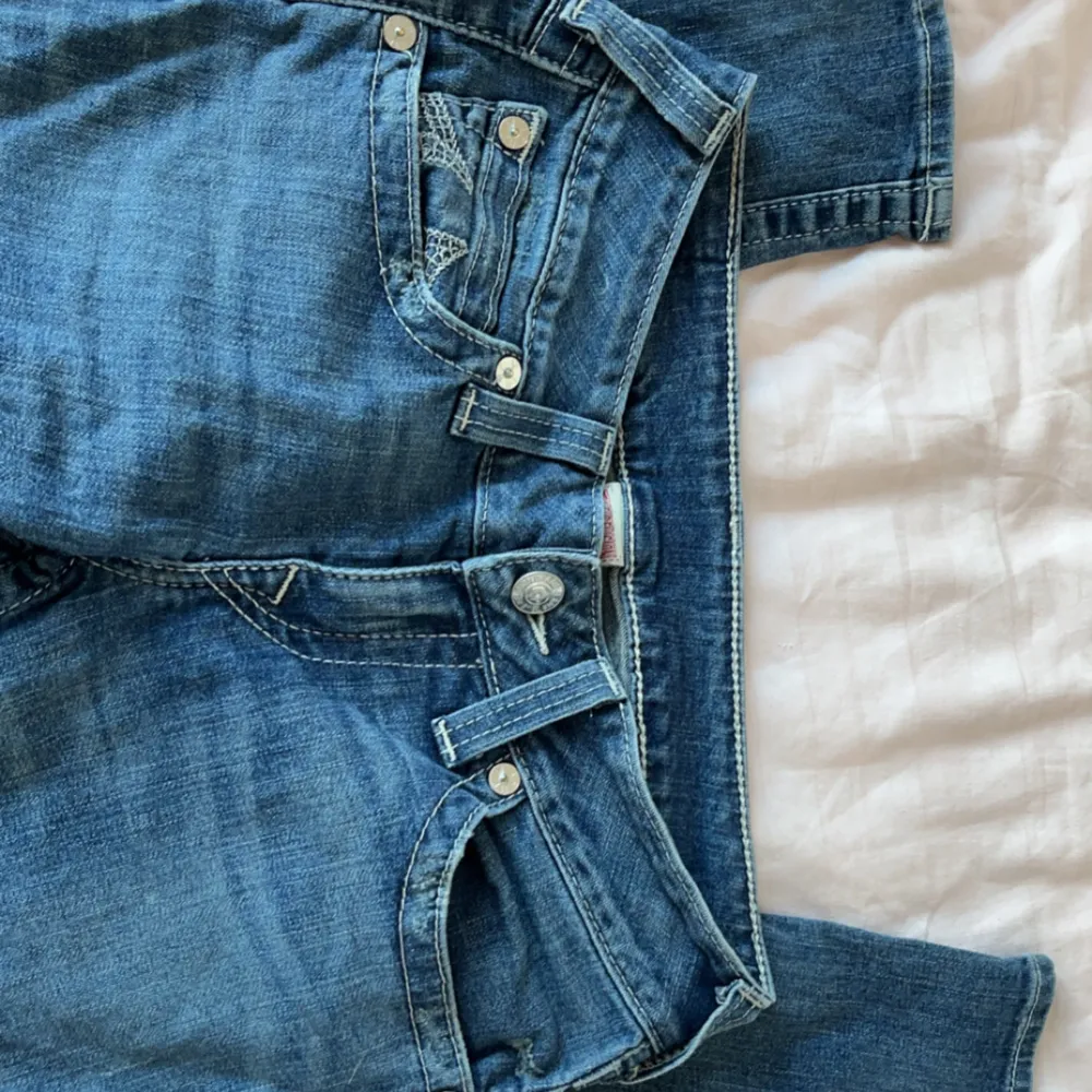 Säljer ett par snygga blå jeans från True Religion i storlek 29. De har ett hål på knät och snygga broderade detaljer på bakfickorna. Perfekta för dig som gillar lågmidjade byxor, dom är skinny men man kan alltid sy om man inte gillar det.. Jeans & Byxor.