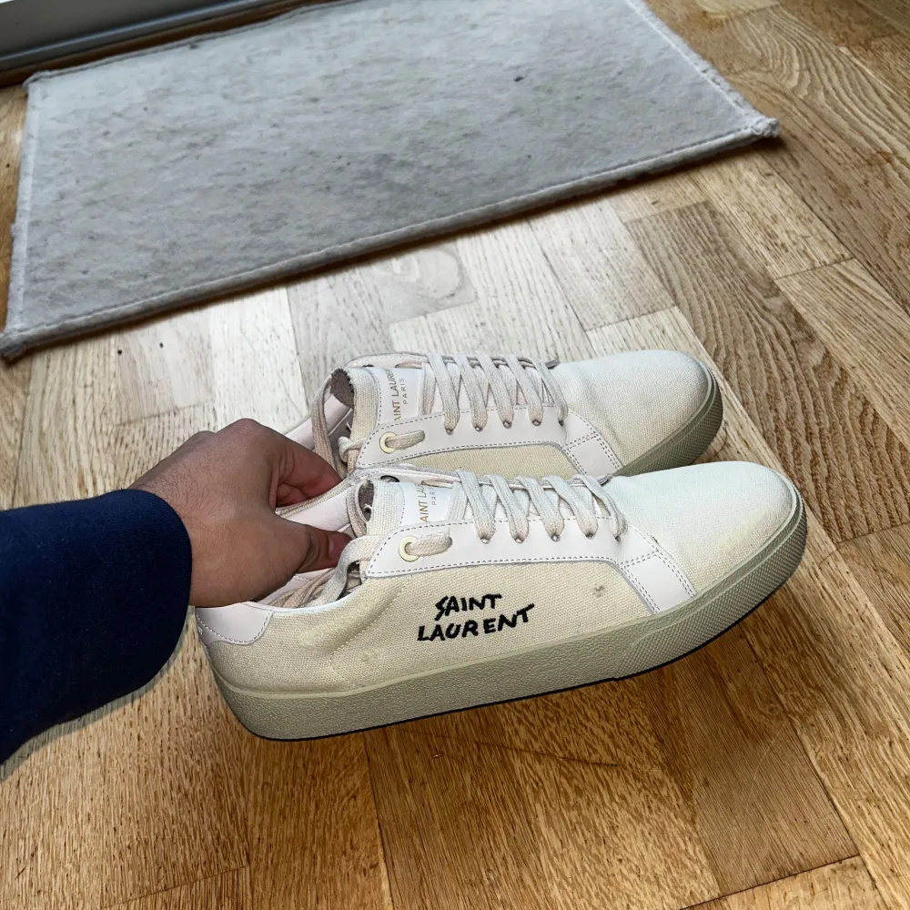 Säljer ett par stilrena vita sneakers från Saint Laurent. De har en klassisk design med snörning och märkeslogga på sidan. Skorna är i mycket bra skick och kommer i originalförpackning. Storlek 41. Säljer för 1999, priset kan diskuteras. Skriv om frågor, säljer då den var för liten på mig. . Skor.