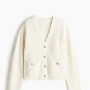 Vit ribbad kofta med knappar - Säljer en superfin vit ribbad kofta med v-ringning och snygga knappar framtill. Den är croppad och har långa ärmar, perfekt för både vår och höst. Koftan har två praktiska fickor fram och är i mycket bra skick. Passar perfekt till både jeans och kjol!