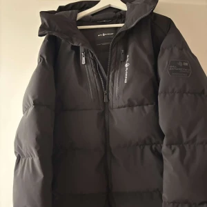 Svart pufferjacka från Sail Racing - Säljer en svart vinterjacka från Sail Racing i storlek L. Jackan har en cool design med dragkedjor och logga på bröstet. Perfekt för kalla vinterdagar med sin varma och quiltade stil. Den är endast använd 1 gång, helt ny säljer den pågrund av att den inte gick att skicka tillbaka 💕