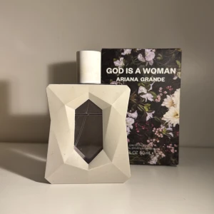 Ariana Grande God Is A Woman Parfym - Säljer en elegant parfymflaska från Ariana Grande, 'God Is A Woman'. Flaskan har en unik geometrisk design i vitt med en avtagbar hållare och en lila tonad vätska. Doften har toppnoter av päron och ambrette, mellannoter av orris och turkisk ros, samt basnoter av madagaskarvanilj och sandelträ. Perfekt för dig som älskar blommiga och varma dofter! Jämförs pris: 650kr