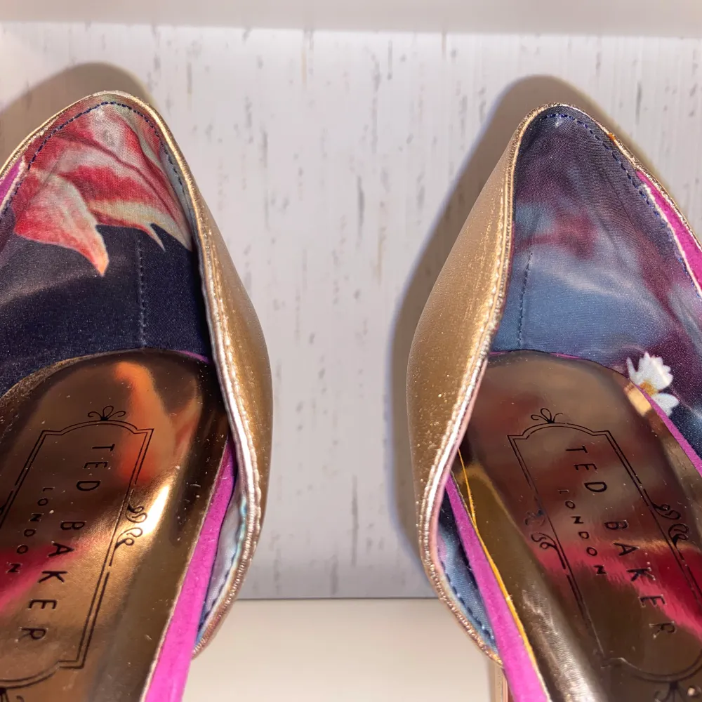 Ted Baker London Suede Heels. Storlek 40. Fuchsia rosa och guld, med spetsig tå och sammetstyg. Blommig design vid hälen och en rosett i roséguld med ett T på baksidan. Klackens höjd: 10,6 cm. Skick: Mycket fint skick. Nypris: 1300 kr. . Kengät.