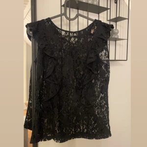 Svart spetsblus med volangdetaljer - Snygg svart spetsblus med volangdetaljer på ärmarna. Perfekt för vardag eller fest! Aldrig använd💗