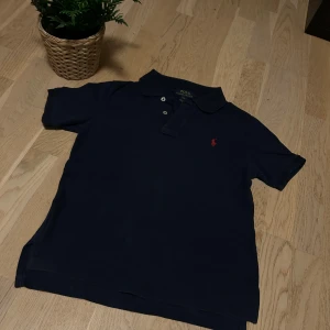 Mörkblå pikétröja från Ralph Lauren - Säljer en klassisk mörkblå pikétröja från Ralph Lauren i storlek S. Tröjan har en broderad röd logga på bröstet och knappar vid kragen. Perfekt för en stilren och avslappnad look. Använd få gånger och i mycket bra skick. Skicka gärna prisförslag. Barn Small inte vuxen.