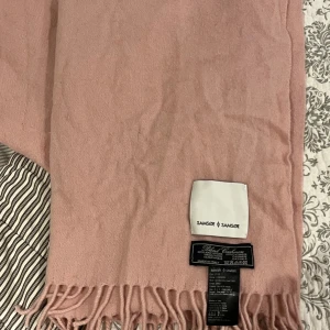 Rosa ullhalsduk från Samsøe Samsøe - Superfin rosa halsduk från Samsøe Samsøe i en mjuk och lyxig blandning av ull och kashmir. Perfekt för att hålla sig varm under kyliga dagar. Den har fransar i ändarna som ger en extra touch av stil. Färgen är en härlig silverrosa som passar till det mesta. Ett måste för höst, vår och vintergarderoben!
