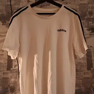 Säljer en vit t-shirt från Adidas i rätt bra skick. Den har klassiska svarta ränder längs axlarna och ett litet Adidas-tryck på bröstet. Perfekt för en avslappnad stil eller träning. Passar både till vardags och sportiga aktiviteter.