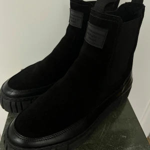 Svarta boots från Gant - Snygga svarta boots från Gant i mocka och skinn. De har en robust sula och en stilren design med elastiska paneler för enkel påtagning. Perfekta för höst och vinter, både till vardags och fest. Märkesdetaljer syns på sidan och sulan. Nypris 2400kr säljs för 1800kr använt dom 3-4 ggr när det var oväder ute 