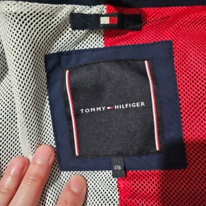 Blå vindjacka från Tommy Hilfiger - Säljer en snygg blå vindjacka från Tommy Hilfiger. Jackan har en dragkedja framtill och är långärmad. Den är perfekt för vår och höst med sitt stilrena utseende och bekväma passform. Detaljer som logotyp på ärmen och insidan av kragen ger den en extra touch. Passar både till vardags och lite finare tillfällen.
