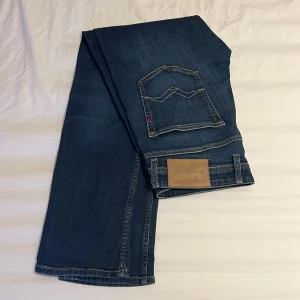 Blå jeans från Replay - Säljer ett par snygga blå jeans från Replay, modell Grover. De har en straight passform och klassisk femficksdesign. Jeansen är i bra skick och perfekta för både vardag och fest. Märkesdetaljer syns på fickan och insidan av midjan. Passar perfekt till en avslappnad stil!