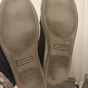 Vinröda  sneakers från Lanvin - Säljer ett par snygga svarta sneakers från Lanvin i mycket bra skick. Skorna har en glansig finish och klassisk snörning. Perfekta för både vardag och fest! Sulorna är i bra skick och skorna är bekväma att bära.