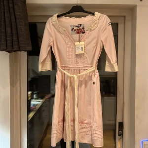 Ljusrosa klänning från Odd Molly - Säljer en superfin ljusrosa klänning från Odd Molly i nytt skick. Den har trekvartsärmar och ett sött knytband i midjan. Klänningen är dekorerad med broderade detaljer och har en romantisk stil. Perfekt för våren eller sommarens fester! 🌸Strl 1/S