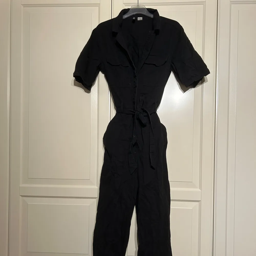 Säljer en svart jumpsuit i bra skick. Den har korta ärmar och ett knytband i midjan för en snygg passform. Materialet känns bekvämt och lätt att bära. . Jeans & Byxor.