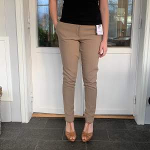 Säljer ett par snygga beige byxor från Selected Femme i storlek 34. De är midwaist och har en slim passform som ger en stilren look. Perfekta för både vardag och fest! Byxorna är i nytt skick med etikett kvar.