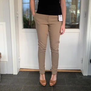 Beige byxor från Selected Femme - Säljer ett par snygga beige byxor från Selected Femme i storlek 34. De är midwaist och har en slim passform som ger en stilren look. Perfekta för både vardag och fest! Byxorna är i nytt skick med etikett kvar.