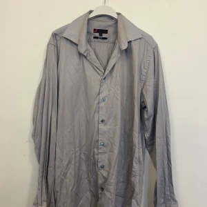 Grå skjorta från Dressmann - Säljer en stilren grå skjorta från Dressmann i storlek L. Skjortan har en slim fit passform och är långärmad med knappar framtill. Perfekt för både vardag och festliga tillfällen. Materialet känns bekvämt och lätt att bära. Passar bra till både jeans och kostymbyxor. 🕺