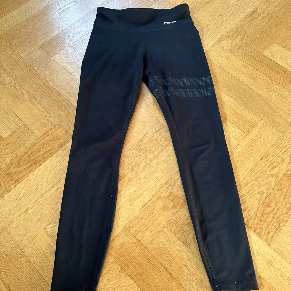 Säljer ett par svarta leggings från Stronger i mycket bra skick. De är högmidjade och har en snygg detalj med två ränder på ena benet. Perfekta för träning eller en avslappnad dag. Materialet är stretchigt och bekvämt.. Jeans & Byxor.