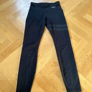 Svarta leggings från Stronger - Säljer ett par svarta leggings från Stronger i mycket bra skick. De är högmidjade och har en snygg detalj med två ränder på ena benet. Perfekta för träning eller en avslappnad dag. Materialet är stretchigt och bekvämt.