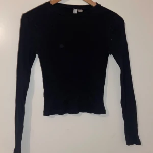 Svart ribbad långärmad tröja - Säljer en stilren svart ribbad tröja med långa ärmar. Perfekt för både vardag och fest. Tröjan är i bra skick och har en tight passform som framhäver figuren. Passar perfekt till höst- och vintergarderoben!