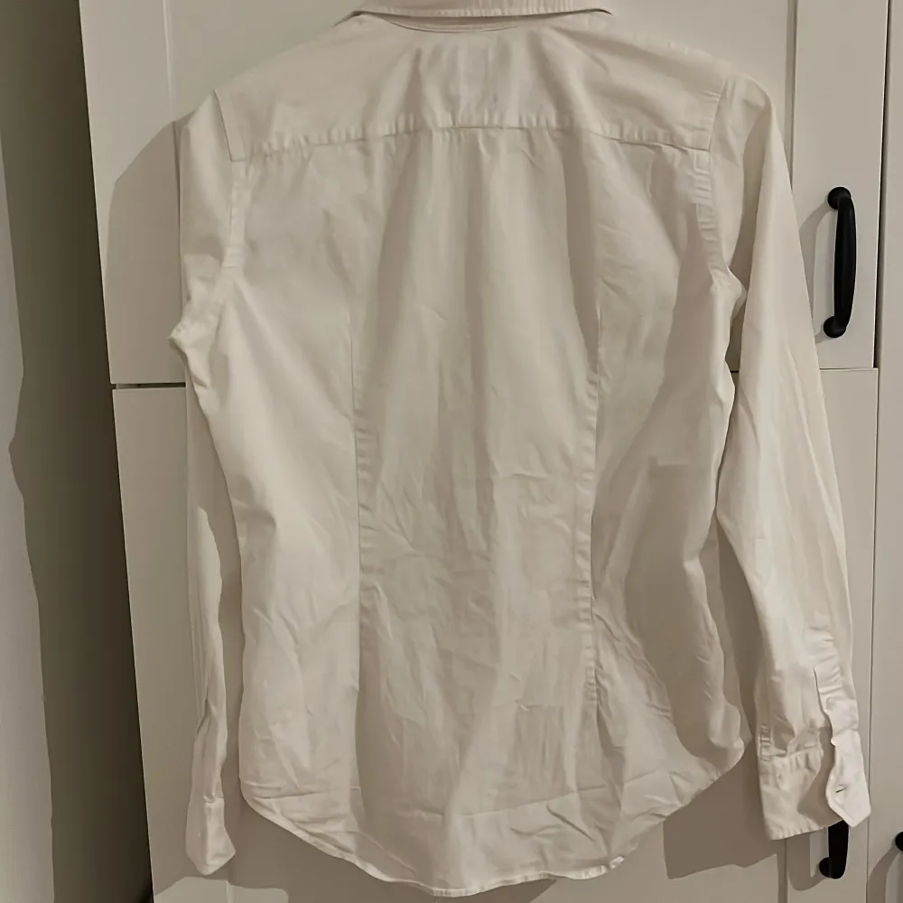 Säljer en stilren vit skjorta från Ralph Lauren i slim fit. Skjortan är i mycket bra skick och har långa ärmar samt knappar framtill. Den är tillverkad i 95% bomull och 5% elastan, vilket ger en skön passform. Perfekt för både vardag och fest! 🕺. Skjortor.