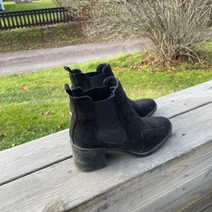 Svarta boots från Divided - Säljer ett par svarta boots från Divided i bra skick. De är gjorda i mocka och har en låg klack. Perfekta för höst och vår, med en stilren design som passar till det mesta. Skorna har en elastisk sida för enkel på- och avtagning. Stl 37