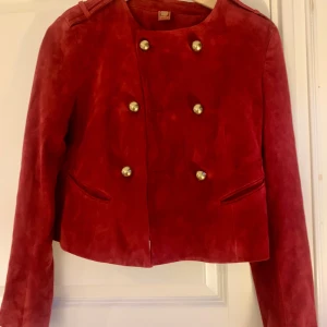 Dondup Röd mockajacka med guldknappar - Säljer en snygg röd mockajacka i mycket bra skick från Dondup. Den har en cool dubbelknäppning med guldknappar och axelremmar som ger en militär look. Jackan är croppad och har långa ärmar. Perfekt för höst och vår när du vill sticka ut lite extra! 🌟Made in Italy stl 42 (Italiens storlek) tror att är 36/38 i svensk storlek. Passar både till jeans eller varför inte över en klänning. Säljer då det är för liten för mig.