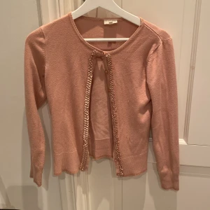 Rosa kofta från POMPdeLUX - Säljer en söt rosa kofta från POMPdeLUX i mycket bra skick. Den har långa ärmar och en fin knytning framtill. Perfekt för vår och sommar när du vill ha något lätt och stilrent. Passar både till vardags och festliga tillfällen. 🌸