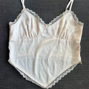 Champagnefärgad topp - Säljer en superfint linne med spetsdetaljer runt kanterna. Den är ärmlös med smala axelband och har en mjuk och skön passform. Perfekt för sommardagar eller som ett lager under en tröja.