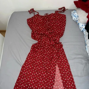 Röd blommig klänning med knytband - Säljer en superfin röd klänning med små vita blommor. Den har knytband vid axlarna och en söt slits framtill. Perfekt för sommarens fester eller en mysig picknick eller ja när som helst när vardagen leker. Klänningen är i bra skick och har en härlig passform. Det är i storlek S och är ifrån Shein 