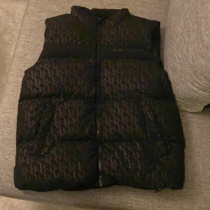 Svart dunväst från Black Squad - Säljer en snygg svart dunväst från Black Squad i storlek L. Västen har ett diskret mönster och dragkedja framtill. Perfekt för höst och vinter, håller dig varm och stilren. Passar både till vardags och lite mer uppklädda tillfällen.