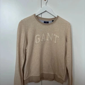 Beige sweatshirt från GANT - Säljer en beige sweatshirt från GANT i storlek M. Tröjan har ett klassiskt tryck med GANT-loggan på bröstet och är i mycket bra skick. Lite smått noppig på loggan, men går att ta bort lätt. Den är långärmad och gjort av bomullstyg