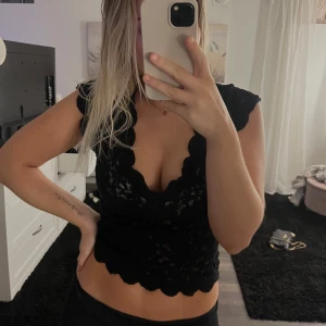 Svart spetstopp - Säljer ett snyggt svart spetslinne med v-ringning och korta ärmar. Toppen är croppad och har en fin volangkant nedtill. Perfekt för en utekväll eller fest! 🖤