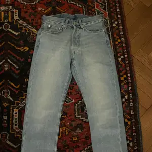 Säljer ett par ljusblå Weekday Pine Regular Tapered Jeans i storlek 27/30. De har en snygg, avsmalnande passform och är perfekta för både vardag och fest. Jeansen är i bra skick och gjorda av skönt denim-material. Perfekta för vår och sommar!