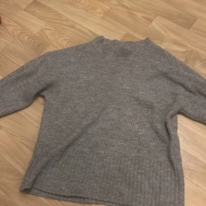 Grå stickad tröja från Lindex - Mysig grå stickad tröja från Lindex för barn i storlek 134/140. Perfekt för kyliga dagar med sin ribbade design och långa ärmar. Tröjan är i bra skick och passar både höst och vinter. Ett måste för garderoben!