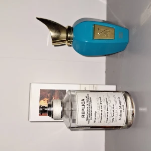 Parfym från Maison Margiela och xerjoff erba pura - Säljer två parfymer: en från Maison Margiela i en genomskinlig flaska med vit etikett och en från Xerjoff i en cool turkos flaska med guldfärgad kork. Maison Margiela-flaskan har en stilren design medan Xerjoff-flaskan har en unik form och lyxig känsla. Perfekt för att uppdatera din doftsamling!