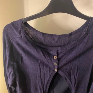 Mörkblå långärmad topp med knappar - Snygg mörkblå topp med långa ärmar och tre dekorativa knappar framtill. Perfekt för både vardag och festliga tillfällen. Materialet känns mjukt och bekvämt mot huden.