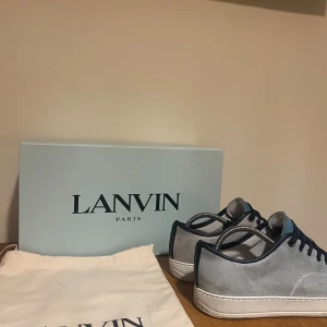  Lanvin sneakers i blått och grått - Snygga Lanvin sneakers i en mix av blått och grått. De har en stilren design med snörning och en vit sula. Perfekta för både vardag och festliga tillfällen. Skorna kommer i originalförpackning med dustbag.