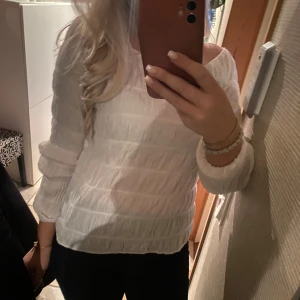 Vit långärmad topp - Säljer en superfin vit långärmad topp med ett subtilt randigt mönster. Perfekt för både vardag och fest! Den är i bra skick och passar perfekt till jeans eller kjol. Skön och stilren design som funkar året runt.