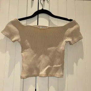 Snygg beige ribbad topp med offshoulder-design. Perfekt för sommardagar eller en avslappnad kväll. Den har en tight passform och korta ärmar som ger en stilren look. Passar bra till både jeans och kjol!