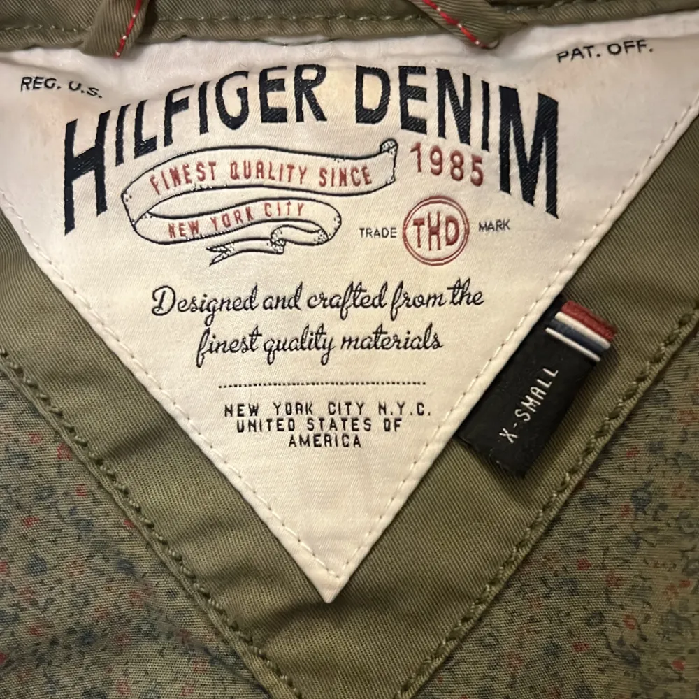 Säljer en snygg grön parkajacka från Hilfiger Denim i storlek XS. Jackan har en praktisk huva och flera fickor med knappar. Perfekt för höst och vår, med en dragkedja framtill och justerbara ärmslut. Superbra skick och redo för nya äventyr! 🍂. Jackor.