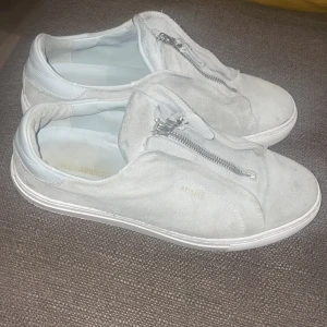 Grå sneakers med dragkedja - Säljer ett par grå sneakers i mocka med dragkedja framtill. De har en stilren design och är perfekta för vardagsbruk. Skorna är i bra skick och har en bekväm passform. Perfekta för både vår och höst!